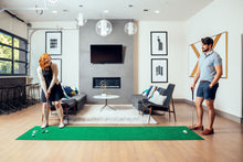 Load image into Gallery viewer, Man and woman couple competing on PUTT-A-BOUT 3x11 Putting Mat in home setting

